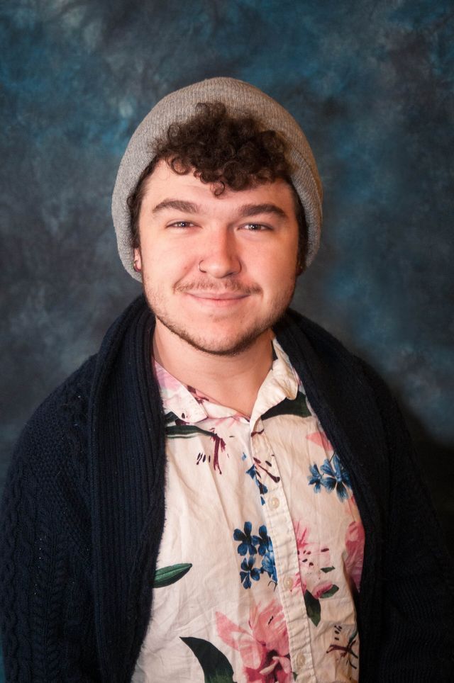 A young man wearing a beanie and a floral shirt is smiling for the camera.