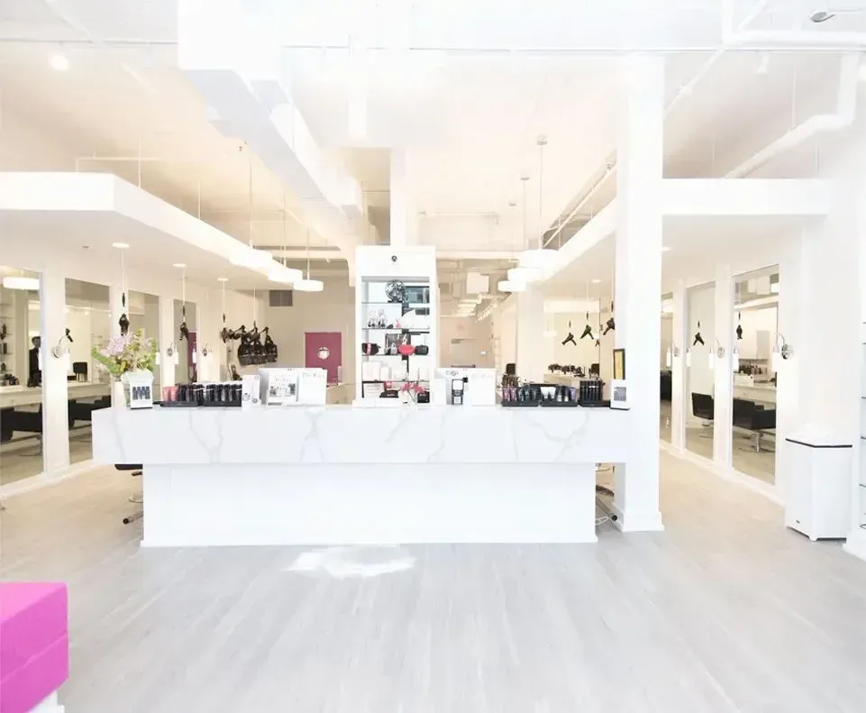 White-walled hair salon with marble-topped reception desk. Stylists and clients reflected in mirrors.