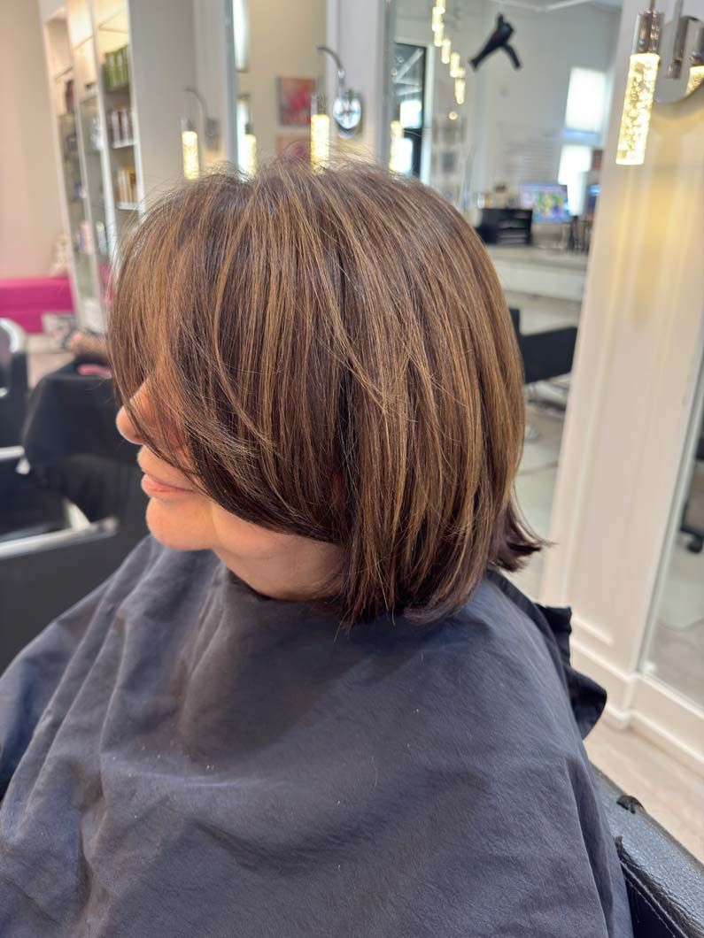 Woman with crimped brown hair at a salon, wearing a salon cape.