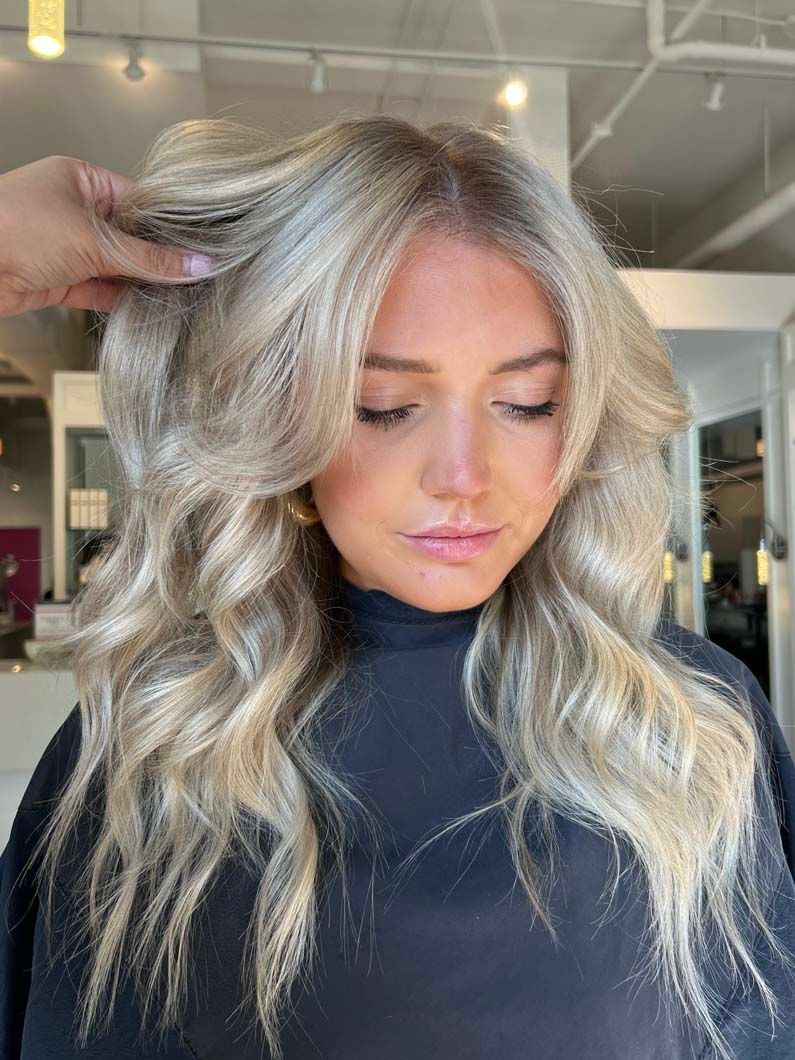 Blonde hair, styled in waves, framing a woman's face in a salon.