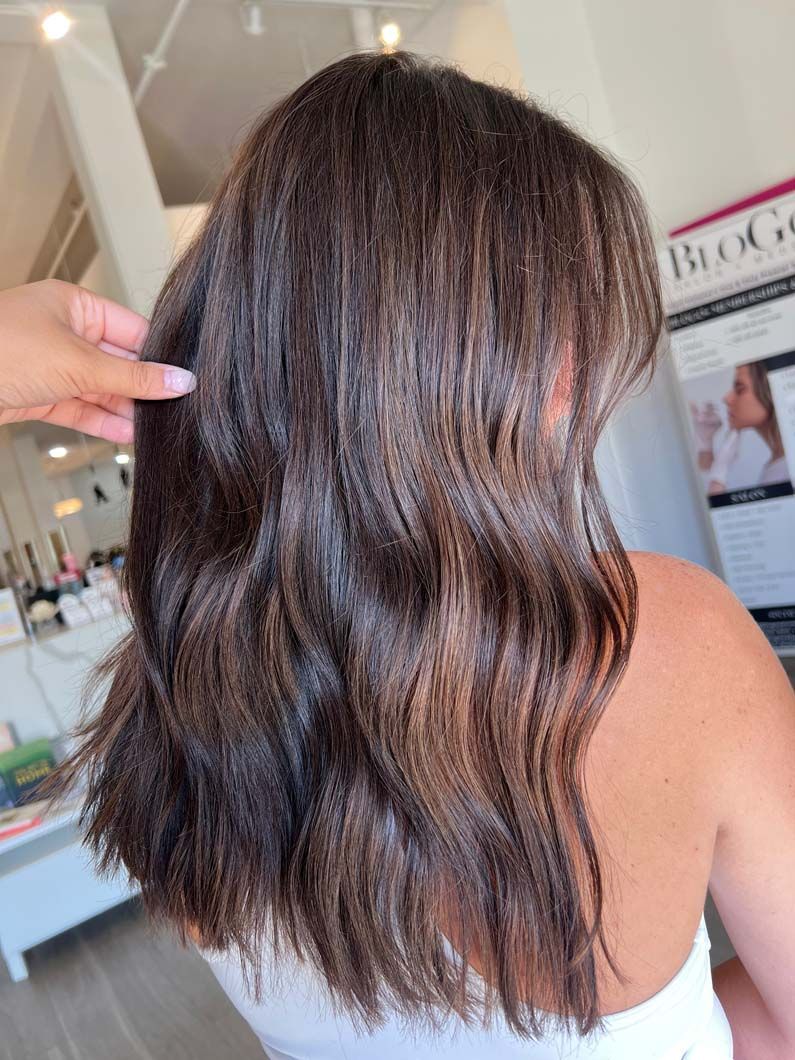 Woman with wavy brown hair, styled in a salon, hand touching the hair.