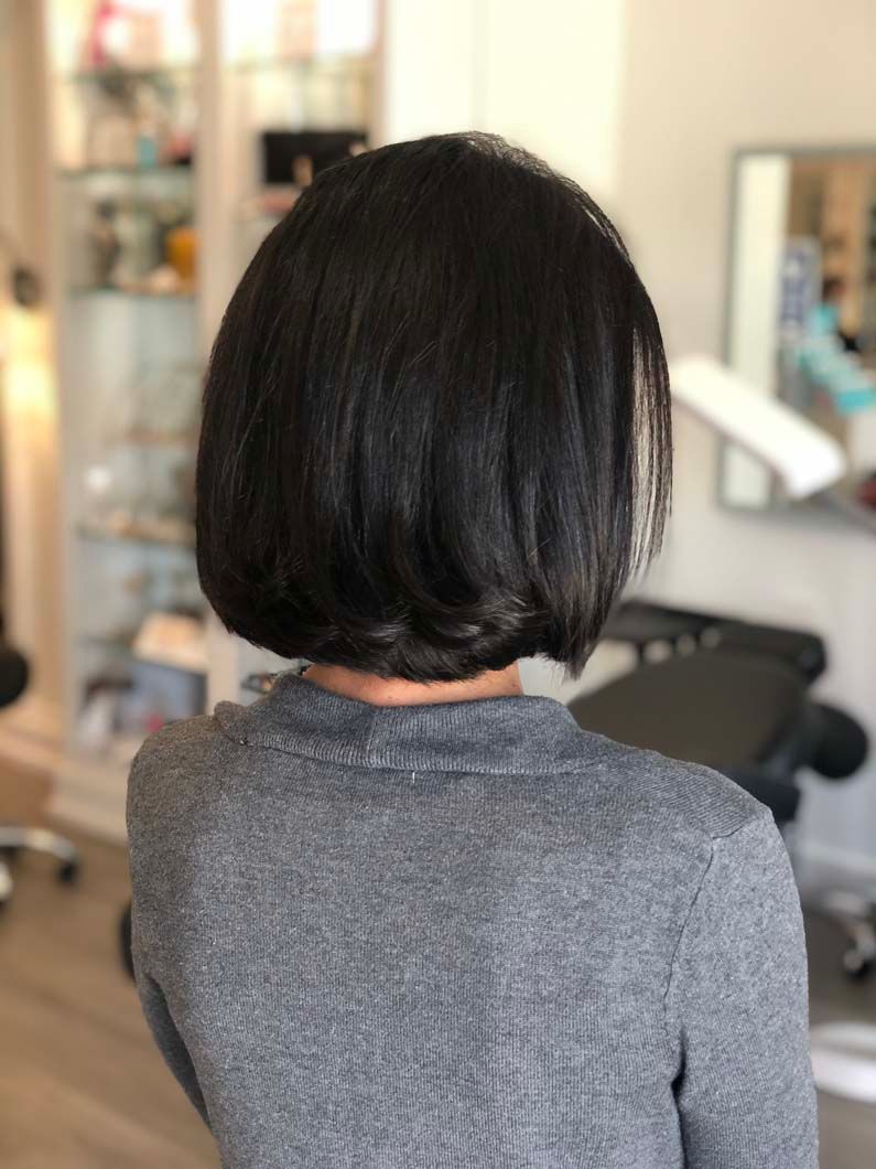 Woman with a layered, dark bob haircut, wearing a gray sweater, standing indoors.