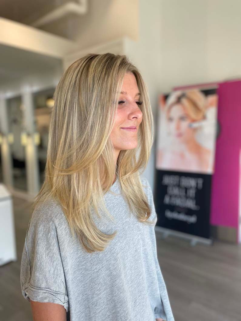 Woman with blonde crimped hair, wearing gray sweater, in a salon, smiling.