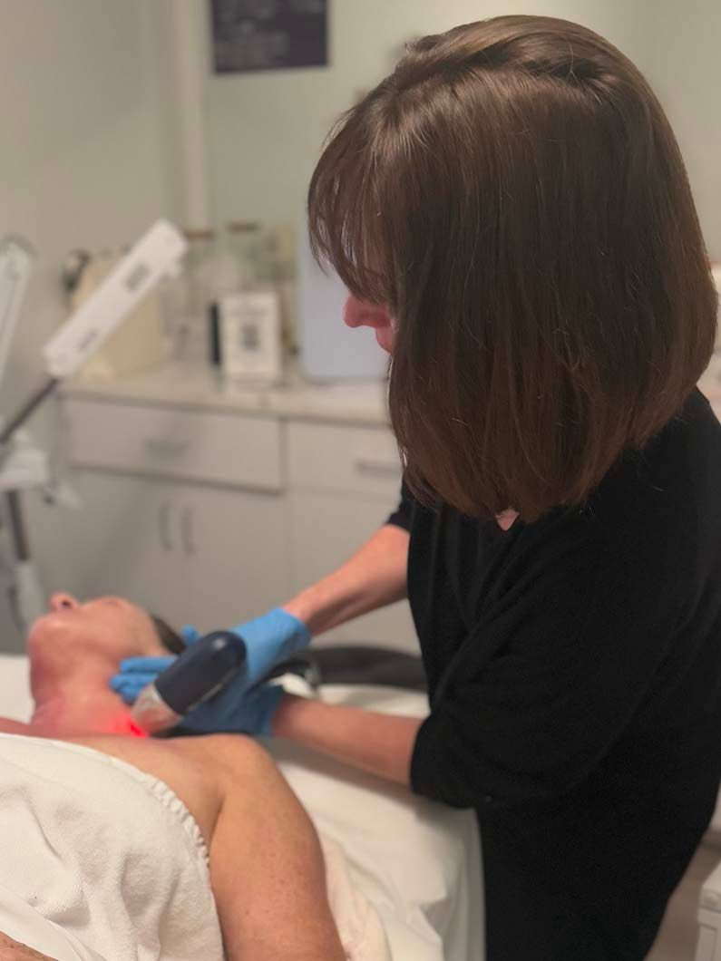 A person receiving laser treatment on their neck at a spa. A technician in blue gloves holds the laser device.
