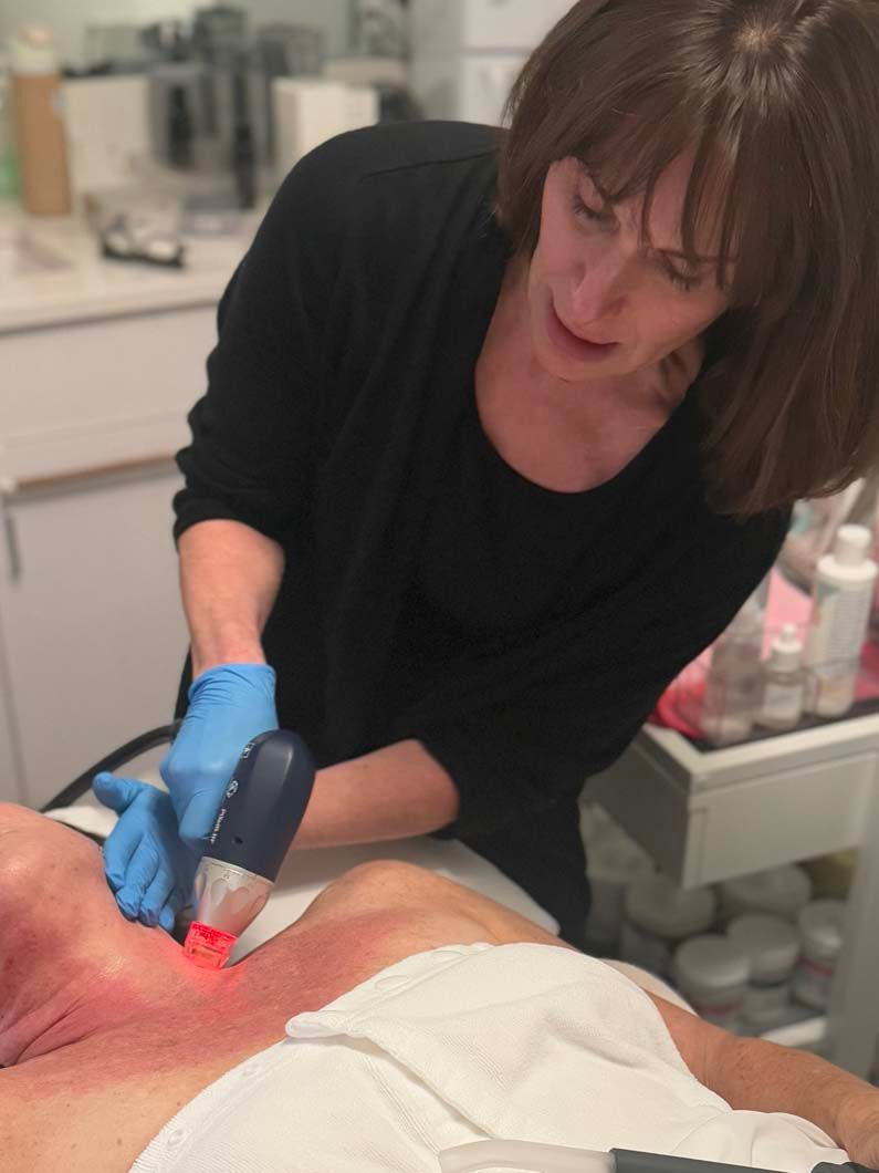 Woman in gloves using a laser device on a person's neck and chest, in a spa-like setting.