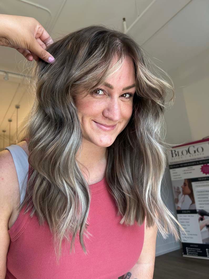 Woman with wavy, highlighted hair, smiling, wearing a pink top.