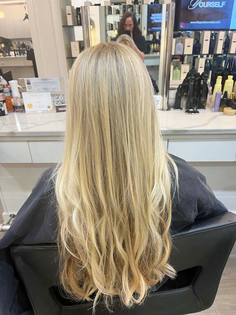 Blonde hair in a salon chair, layered cut, looking at a mirror with a hairstylist.