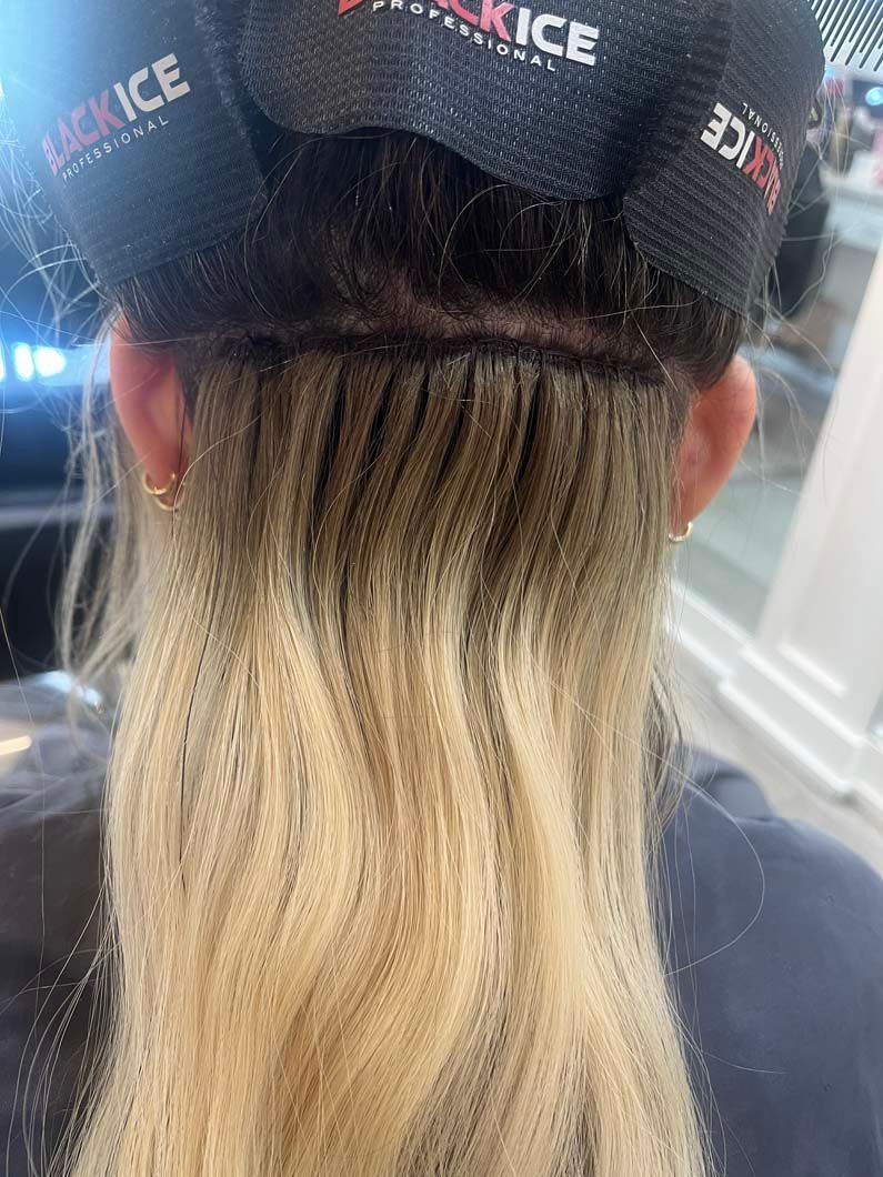 Back view of a person with blonde hair, visible hair extensions, and black hair rollers.