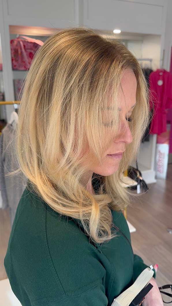 Woman with layered blonde hair, looking down in a shop. She wears a green sweater.