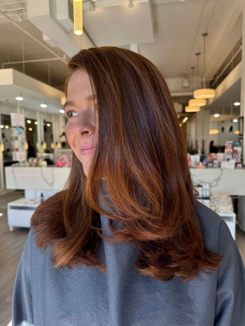 Woman with reddish-brown crimped hair, wearing a gray sweater, indoors at a salon.