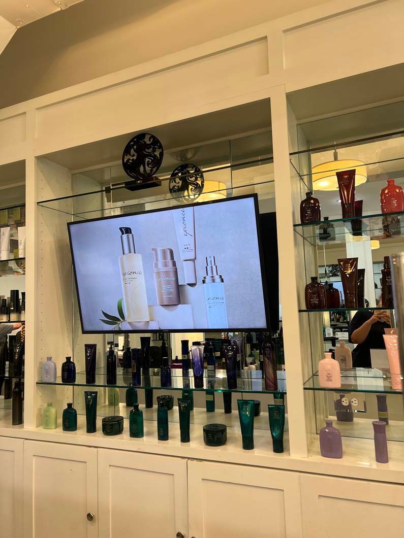 Display of beauty products with a TV screen above displaying products. White shelving, green, black and pink packaging.