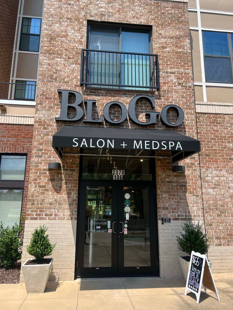 Exterior of Blogo Salon + Medspa with awning over glass door entrance and brick facade.