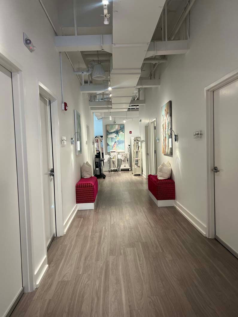Hallway with white walls, wood floors, and doors on either side. Red benches and art pieces are visible.