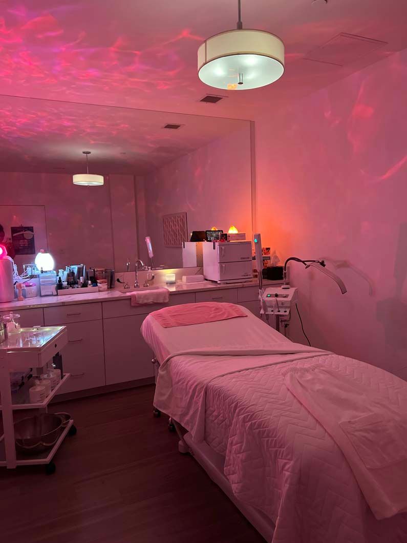 Spa treatment room with pink lighting, bed, and equipment.