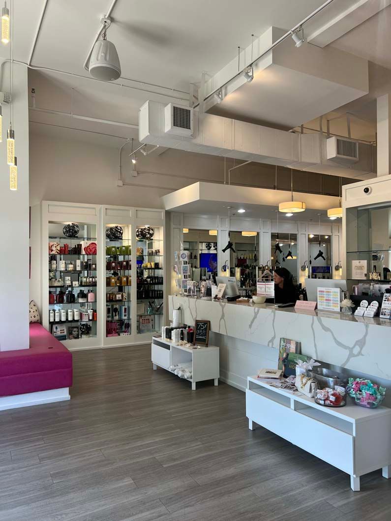 Salon interior with products displayed. Reception area with a woman at the desk. Pink bench.