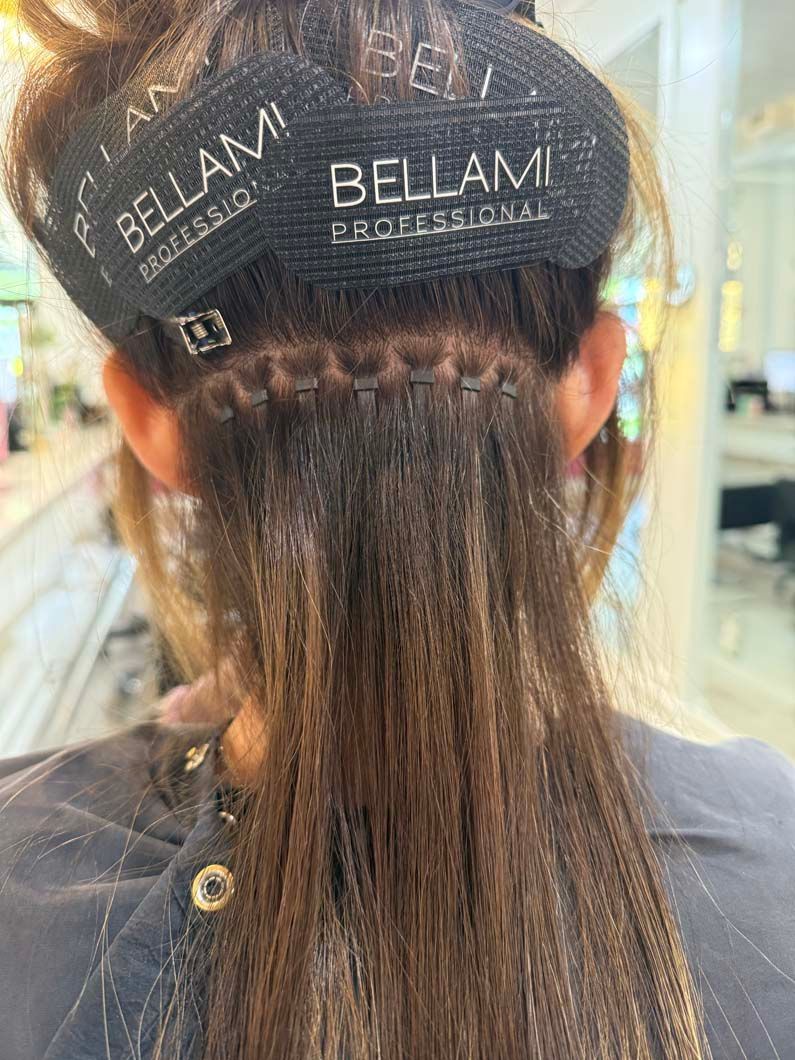 Close-up view of a person's hair with Bellami hair extension wefts attached near the scalp.
