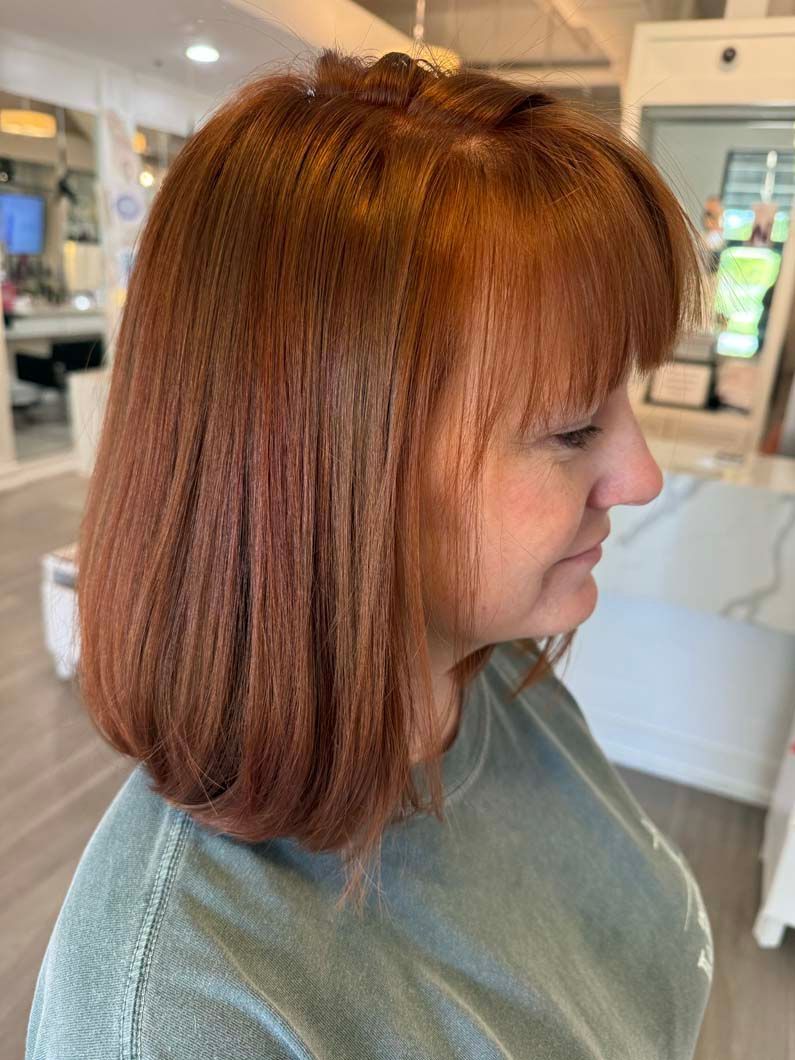 Woman with red, crimped hair and bangs, in a salon, looking to the side. Wearing a green shirt.