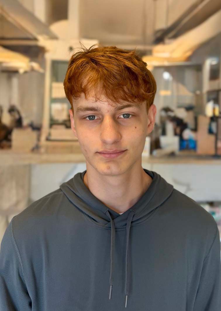 Young person with red hair wearing a grey hoodie, looking at the camera. Neutral background.