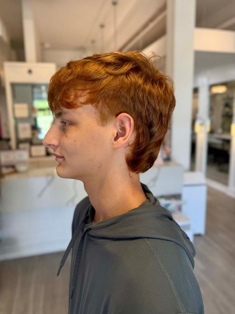 A person with red hair wearing a gray hoodie, facing left, inside a building.