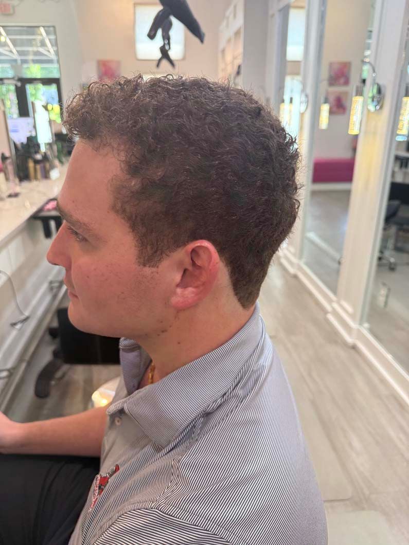 Man with brown curly hair in a salon, wearing a striped shirt.