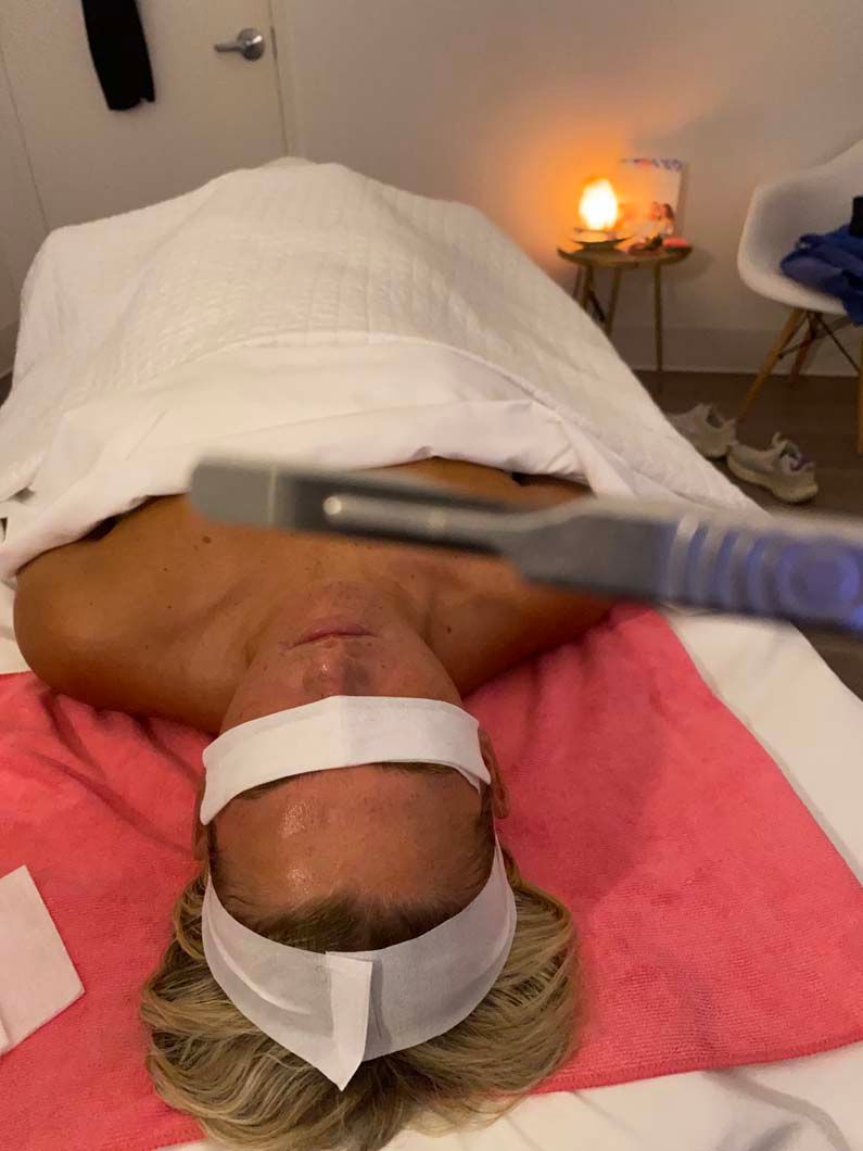 Person lying on massage table with a scalpel held above their face. White towel, blindfold, pink sheet.