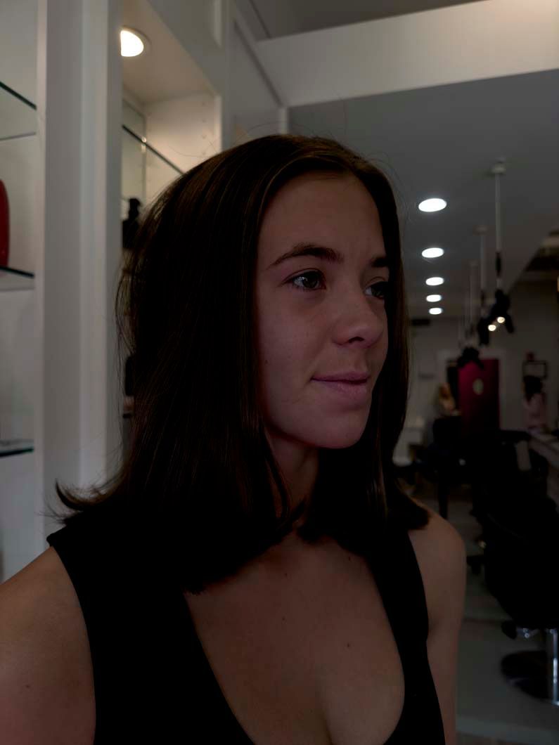 Woman with dark hair, looking right, in a salon. Wearing black top.