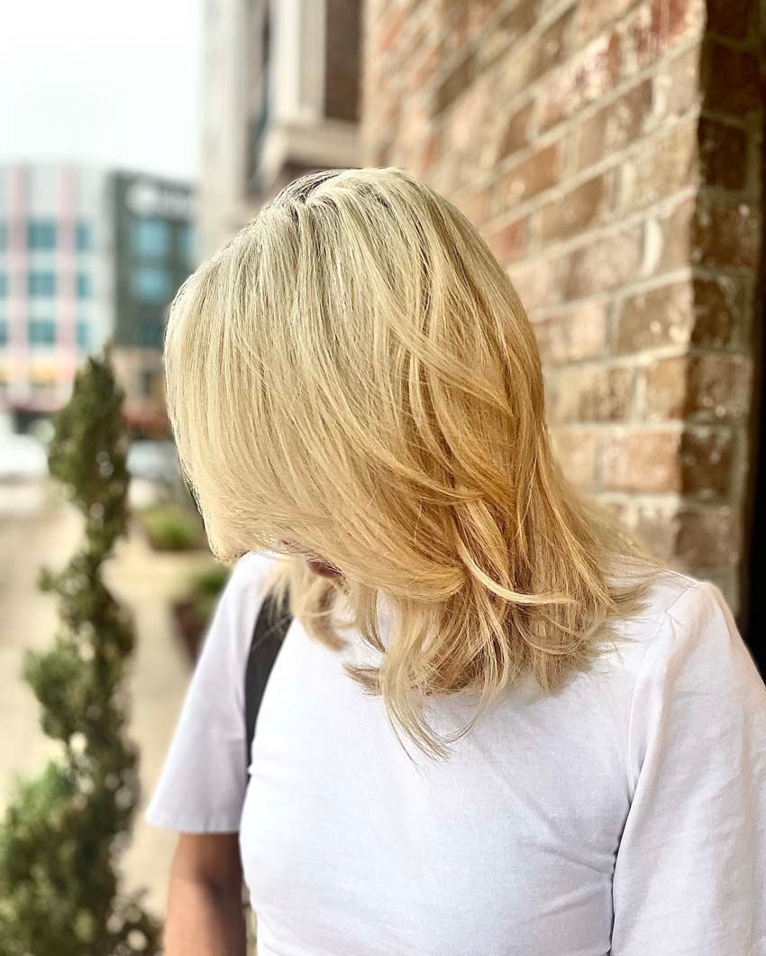 Blonde hair, white shirt, brick wall background, outdoors.