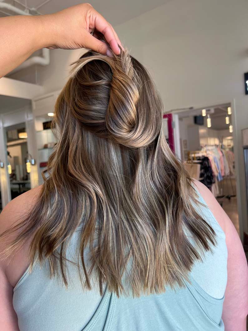 Woman with wavy brown and blonde hair, partially styled in a twisted updo.  A hand holds the styled section.