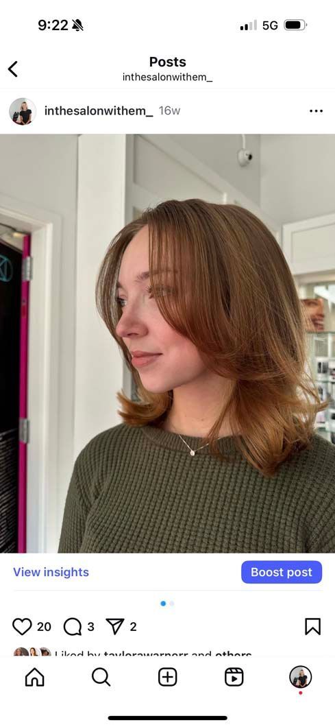 Woman with layered brown hair and a green sweater stands in front of a white wall, side profile.