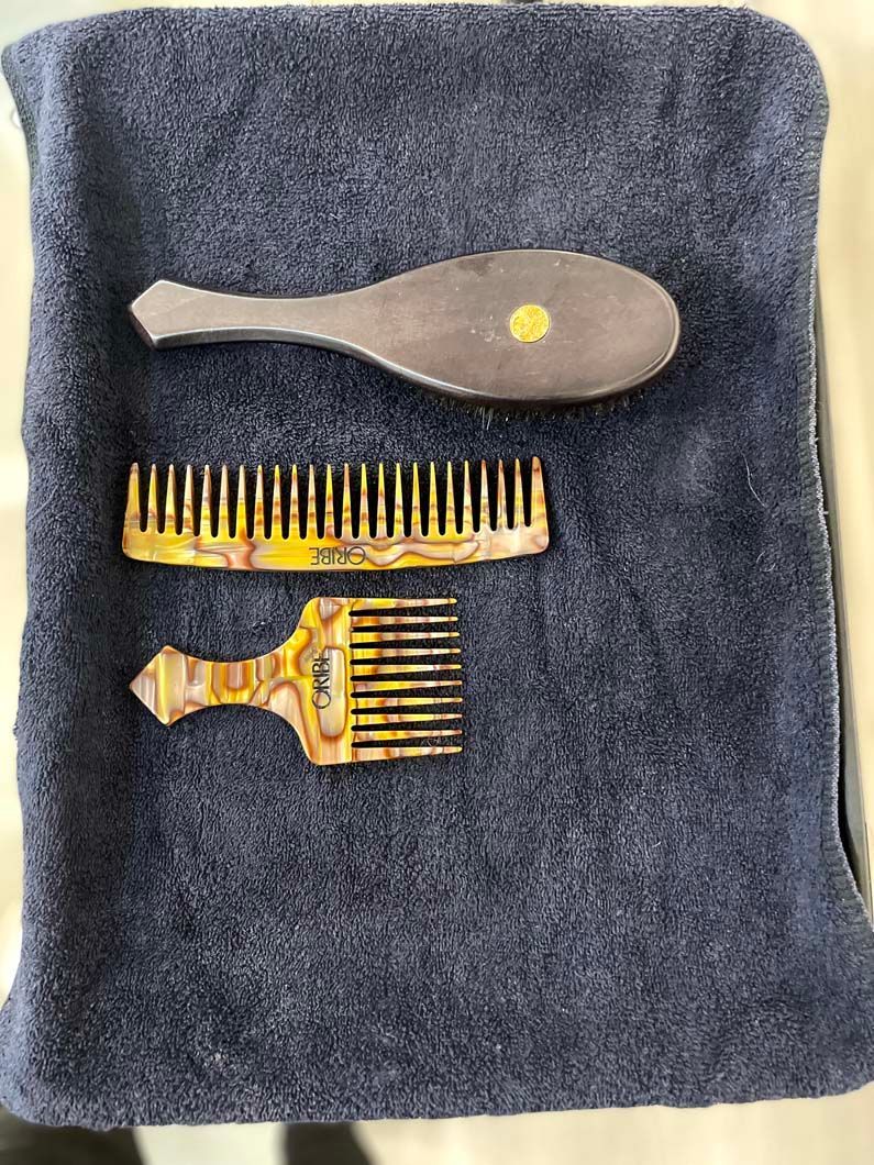 Three hair combs on a dark blue towel: a brush, a wide-toothed comb, and a pick comb.