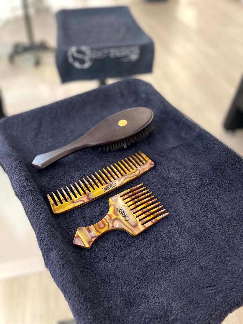 Hairbrushes and combs on a dark blue towel, set on a stool in a salon.