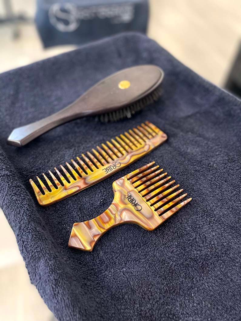 Hair styling tools on a dark blue towel: brush, wide-tooth comb, and pick comb.