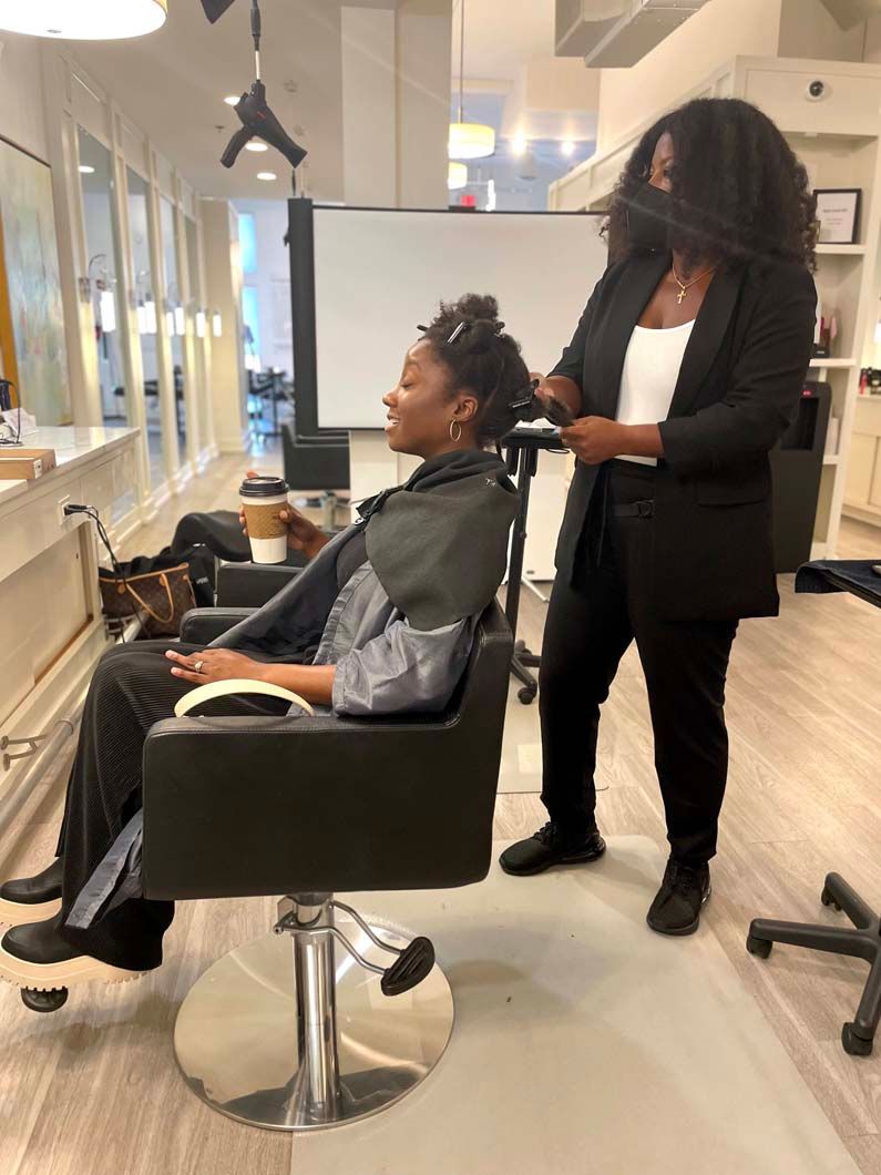 Hair stylist working on client's hair in a salon. Client seated, wearing a salon cape.