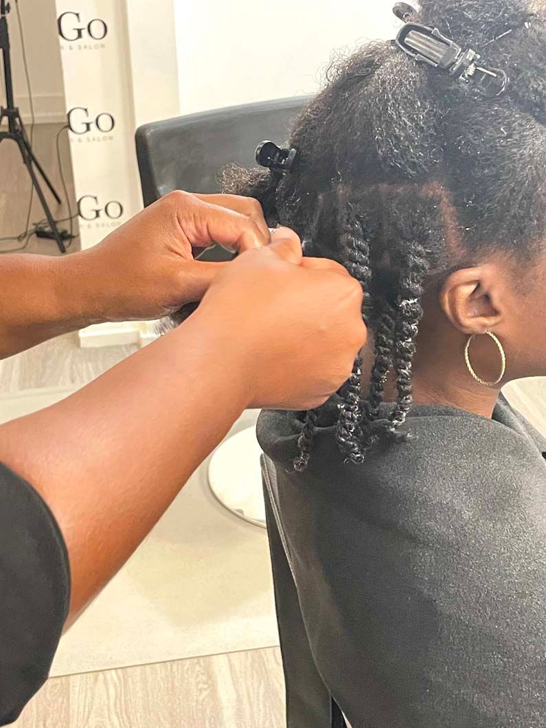 Hands twisting wet hair into coils in a salon. Hair is dark and the person has hoop earrings.