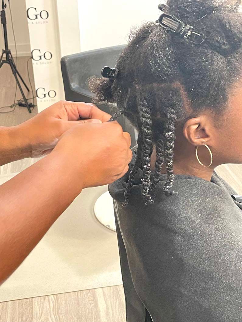 Hands twisting natural hair into coils, in a salon setting.