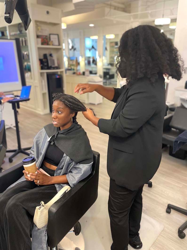 Woman in salon chair, stylist adjusting her hair. The salon is bright and airy.