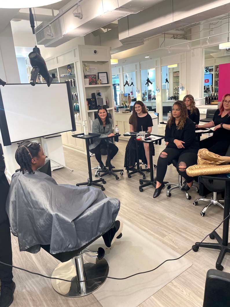 A hair styling demonstration in a salon. Stylists watch as a model receives a hair treatment.