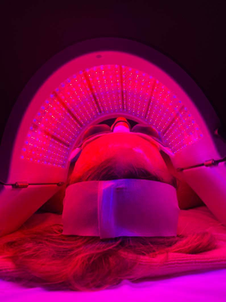 Person lying under a red LED light therapy machine.