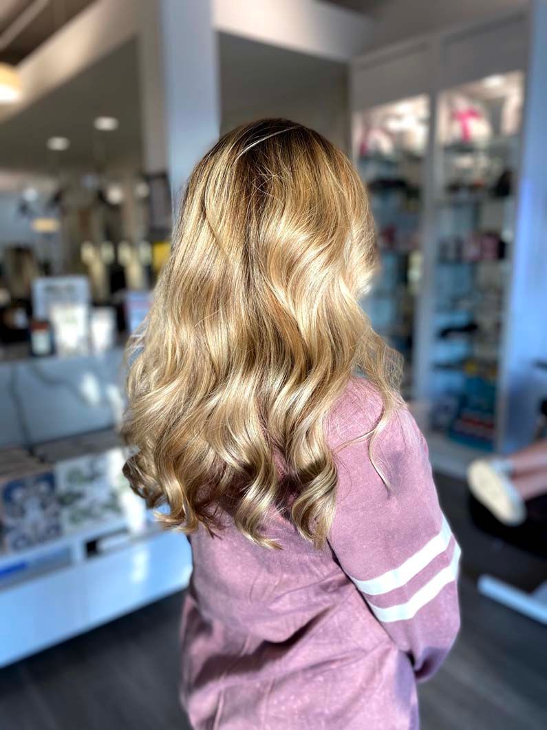 Woman with wavy, light brown hair wearing a pink sweater. She is in a store.