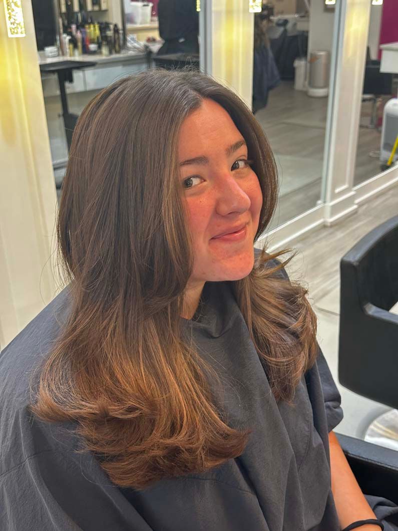 Woman with brown hair styled with layers and ombre coloring, smiling in a salon.