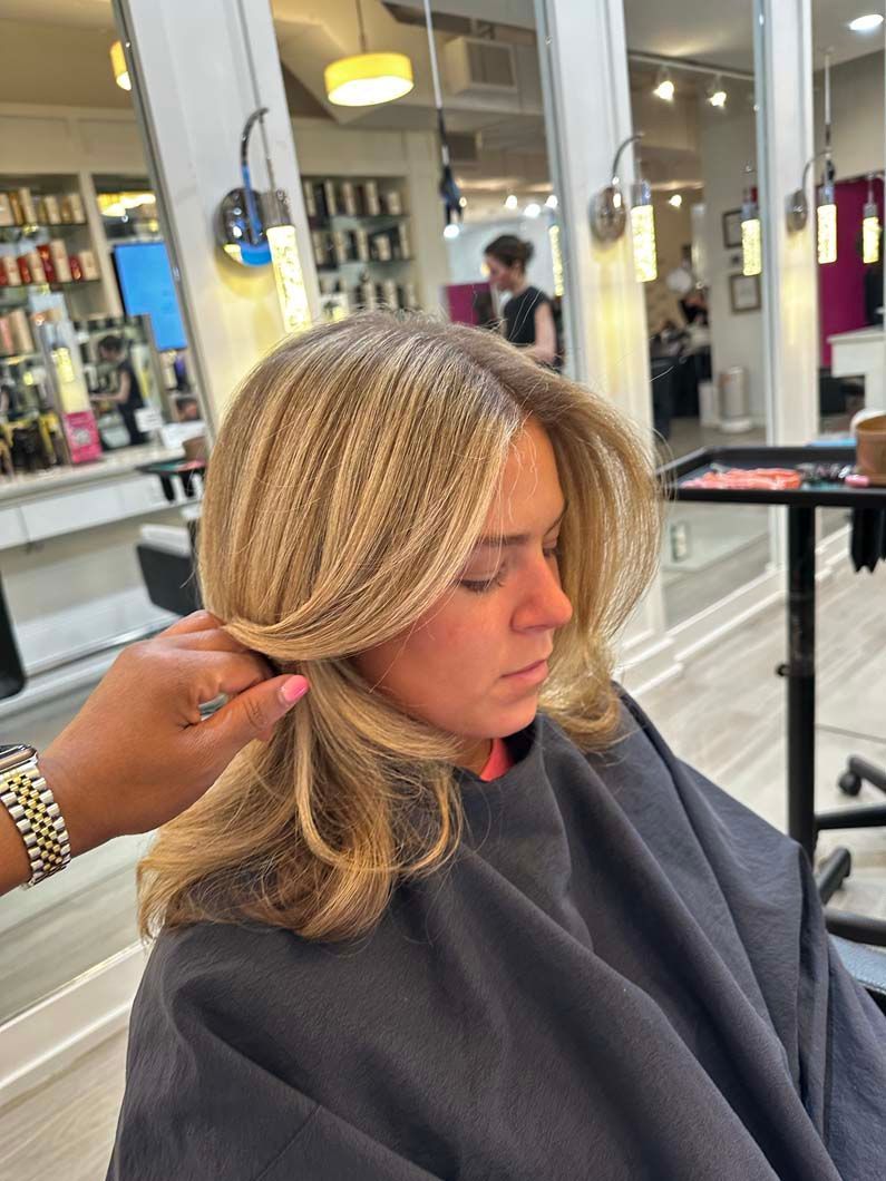 Woman with blonde hair receiving hair treatment in a salon. Stylist's hand holding hair.