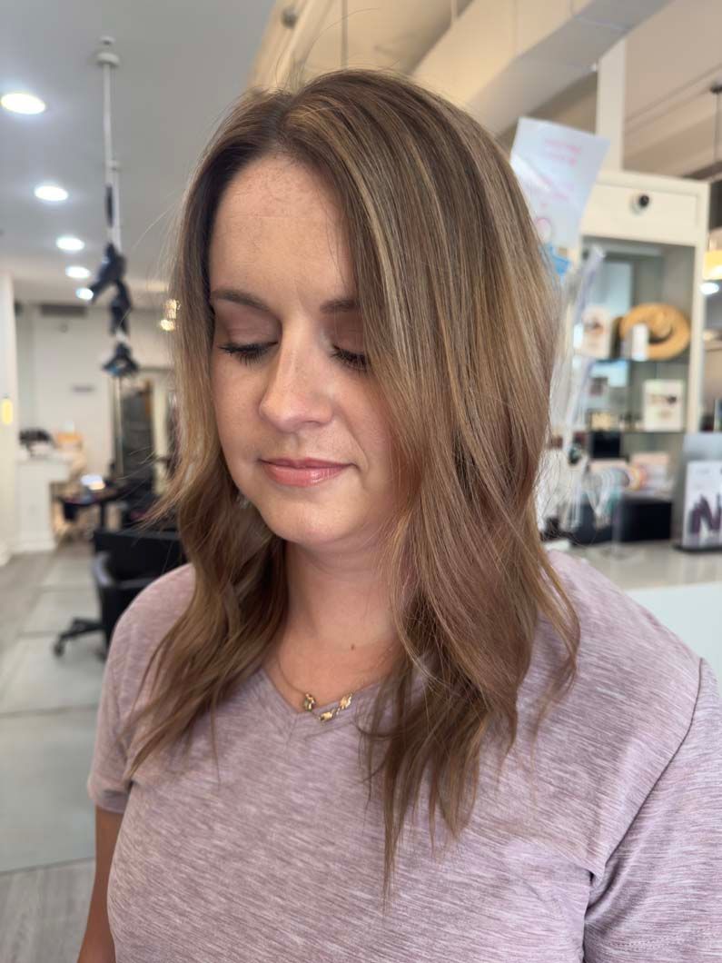 Woman with layered, highlighted brown hair, soft waves, and a pink shirt in a salon.