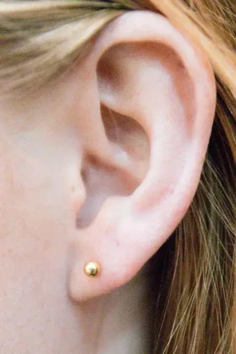 Close-up of a person's ear with a small gold stud earring in the lobe.