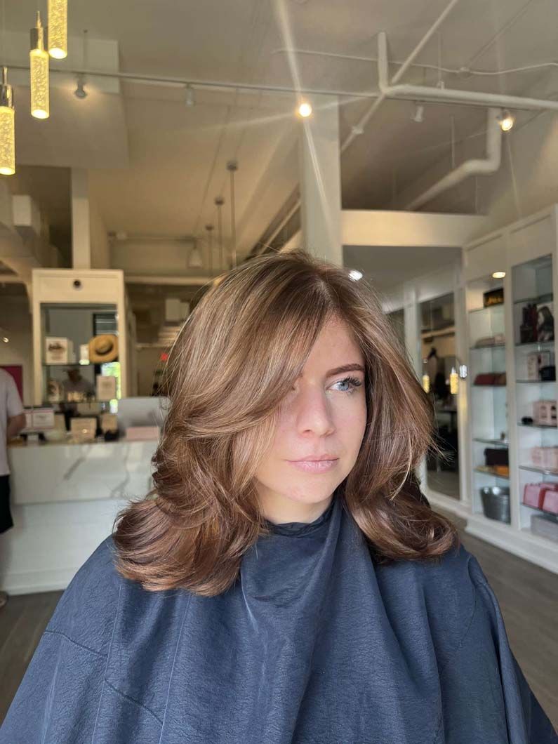Woman with layered brown hair in a salon, wearing a black cape.
