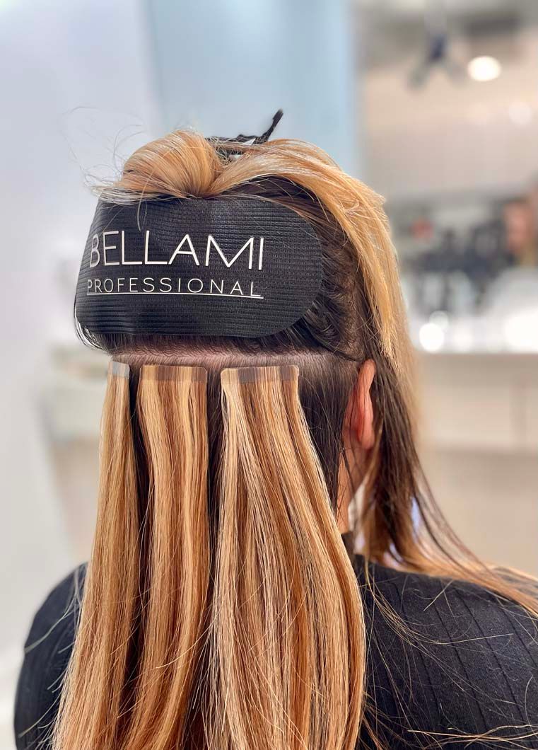 Person with blonde hair receiving hair extensions at a salon.