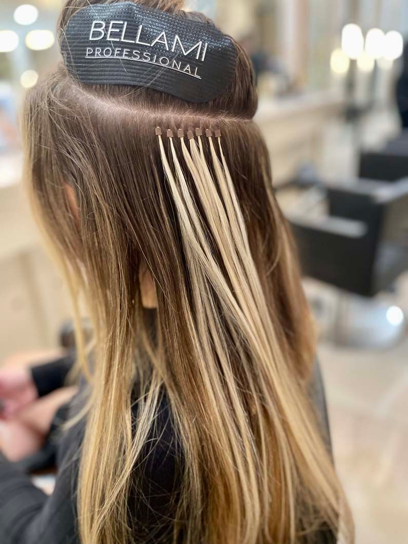 Hair extensions being installed, showing attachment points, with a blonde and brown color gradient.