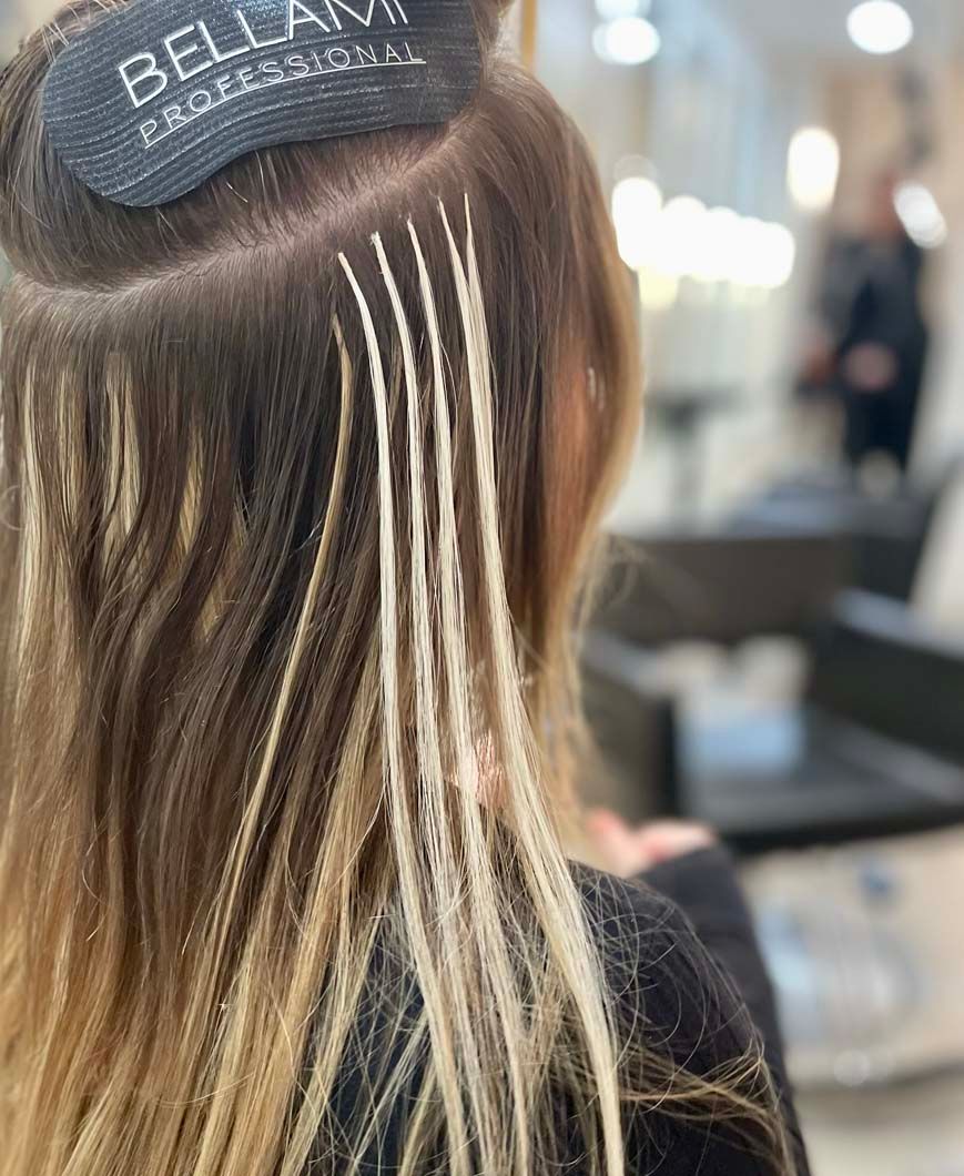 Hair extensions being installed in a salon; blonde and brown hair with visible attachment points.