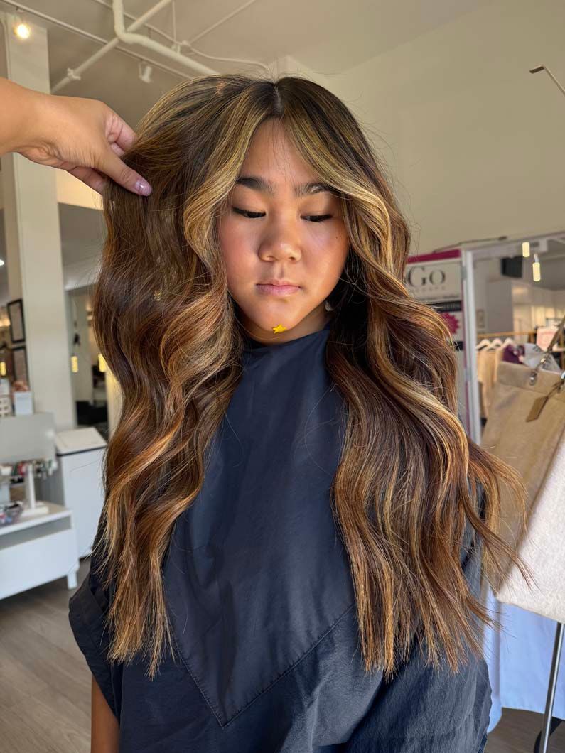 Woman with wavy brown hair with blonde highlights styled at a salon.