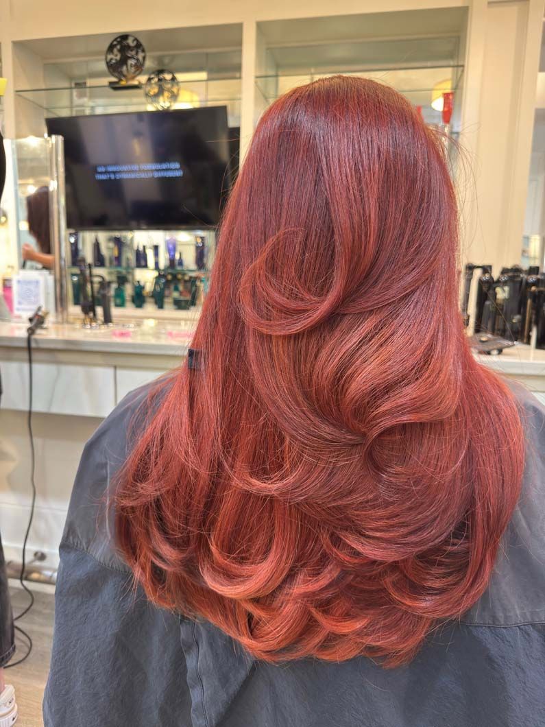 Person with long, red layered hair at a salon.