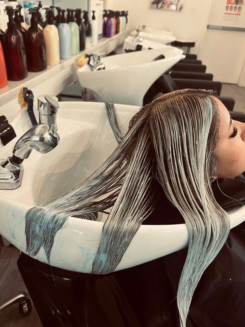 Person having hair treatment at salon sink. Hair is covered in a light blue substance.